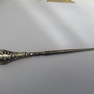 May include: A silver shoe horn with an ornate handle. The handle is shaped like a teardrop and has a floral design.