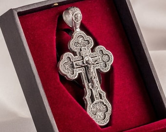 May include: A silver cross pendant with intricate details, including a figure of Jesus Christ, is displayed in a black velvet-lined box with a red interior.