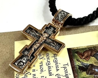 May include: A silver and gold cross pendant with intricate details and religious imagery. The cross is attached to a black cord necklace with gold beads.