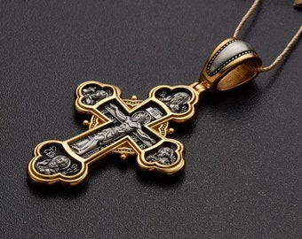 May include: A silver and gold cross pendant with black enamel and detailed engravings. The cross features a depiction of Jesus Christ on the front and four saints on the sides.