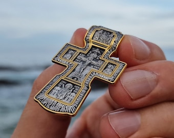 May include: A silver and gold cross pendant with intricate details and religious iconography. The cross is decorated with small images of saints and religious symbols.