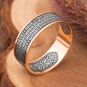 Könnte beinhalten: Ein goldener Ring mit einer schwarzen Inschrift in einer alten Sprache. Die Inschrift befindet sich auf der Außenseite des Rings und die Innenseite des Rings hat ein schwarzes Kreuzdesign.