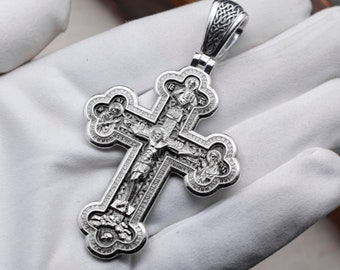 May include: A silver Orthodox cross pendant with intricate details and multiple figures. The cross is highly detailed and has a textured surface.