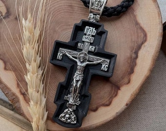 May include: A black wooden cross with a silver Jesus figure. The cross has Cyrillic lettering on it. The cross is on a wooden surface.