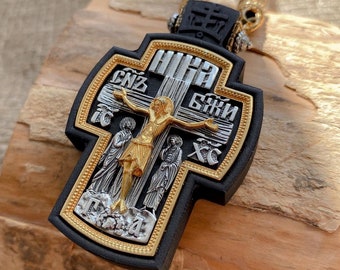 May include: A black wooden cross with gold and silver accents. The cross features a depiction of Jesus Christ on the cross with the words "Иисус Христос" (Jesus Christ) in Cyrillic script. The cross is decorated with a gold border and a gold and silver pattern.