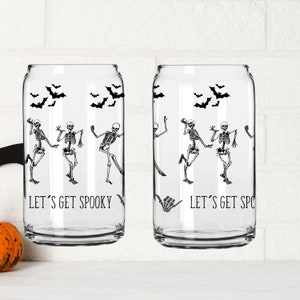 May include: Two clear glass can-shaped cups with black skeleton designs and the text "Let's Get Spooky" printed on them.