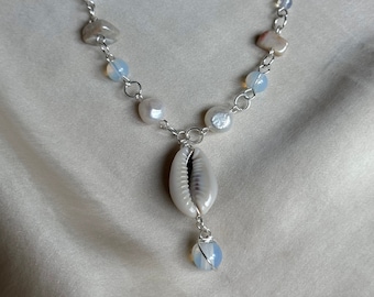 May include: A silver chain necklace with white and brown beads, a white seashell pendant, and a blue opal drop.