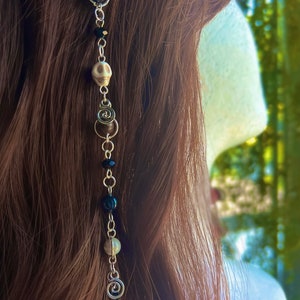 May include: A silver chain hair accessory with black, brown, and white beads, including a skull charm and a spiral charm.