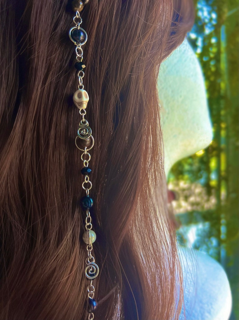 May include: A silver chain hair accessory with black, brown, and white beads, including a skull charm and a spiral charm.