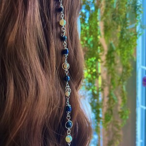 May include: A silver chain with blue and yellow beads and a dragonfly charm. The chain is hanging from a person's hair.