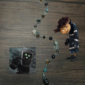 May include: A silver chain necklace with a black stone pendant. The chain features various beads, including black, brown, blue, and green. The necklace is on a wooden surface.