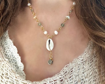 May include: A gold chain necklace with white and green beads and a white seashell pendant. The pendant has a gold ring with a green stone hanging from it.
