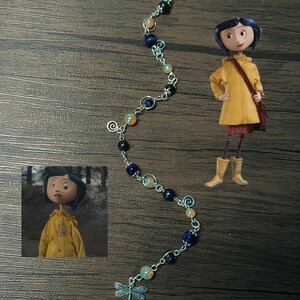 May include: A silver chain bracelet with blue, black, and orange beads and a dragonfly charm. The bracelet is on a wooden surface.