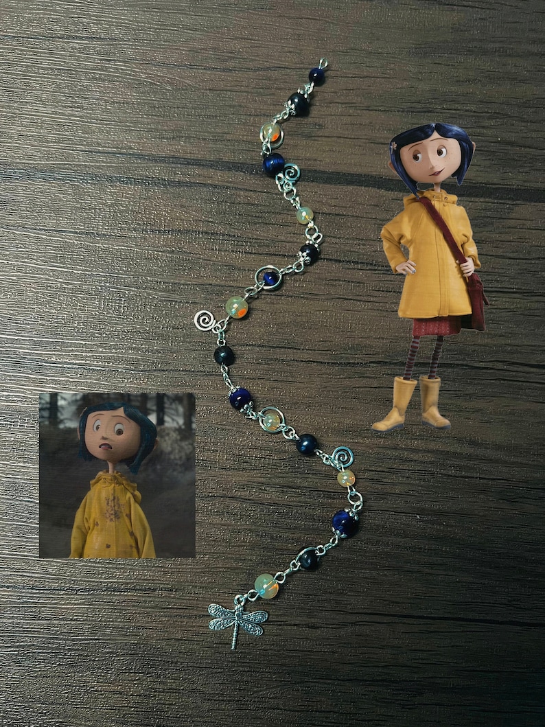May include: A silver chain bracelet with blue, black, and orange beads and a dragonfly charm. The bracelet is on a wooden surface.
