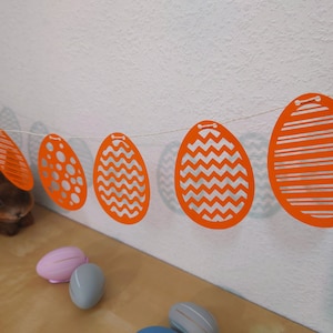 Può includere: Ghirlanda pasquale festosa con sagome di uova di Pasqua in carta arancione con diversi motivi.
