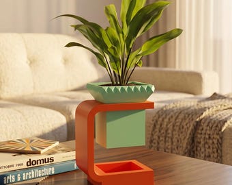 May include: A green potted plant sits in a light green square planter with a serrated top edge, supported by a bright orange C-shaped stand. The planter is suspended above a matching orange square base, creating a floating effect for the greenery.