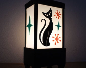 May include: A black and white lamp with a silhouette of a cat and geometric shapes. The lamp has a white frosted glass shade and a black base.