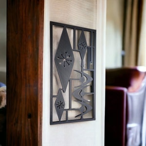 May include: A black metal wall decor with a geometric design featuring diamonds, boomerangs, and stars. The decor is mounted on a white wall.