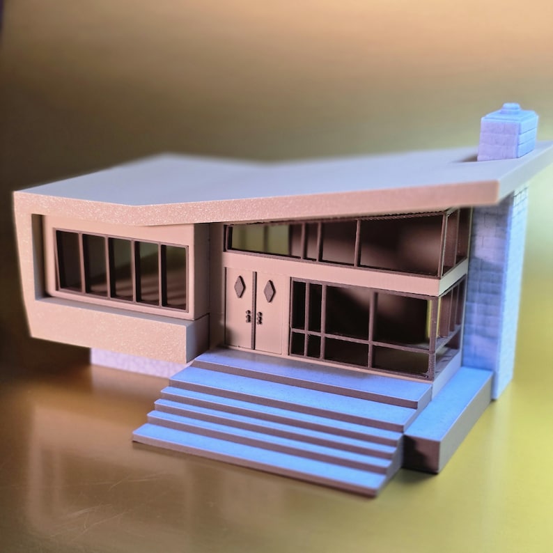May include: A 3D printed model of a modern house with a flat roof, a chimney, and a set of stairs leading to the front door. The house is painted in shades of gray and blue.