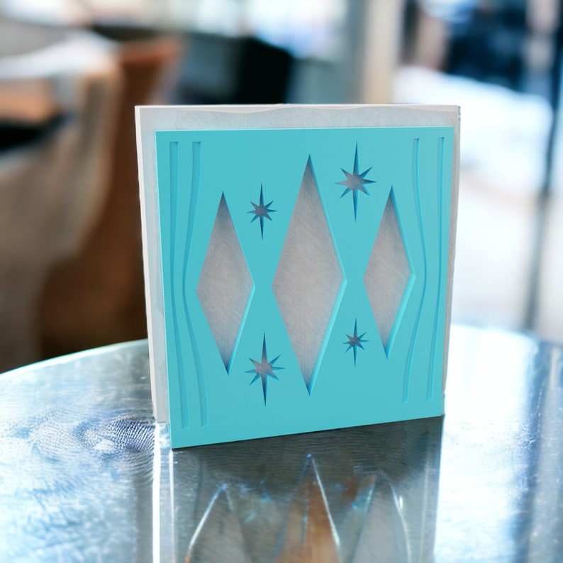 May include: A square decorative panel featuring a bright turquoise front layer with cutouts of three vertical diamonds and four starburst shapes, layered over a solid white backing, creating a geometric design with clean, sharp edges.