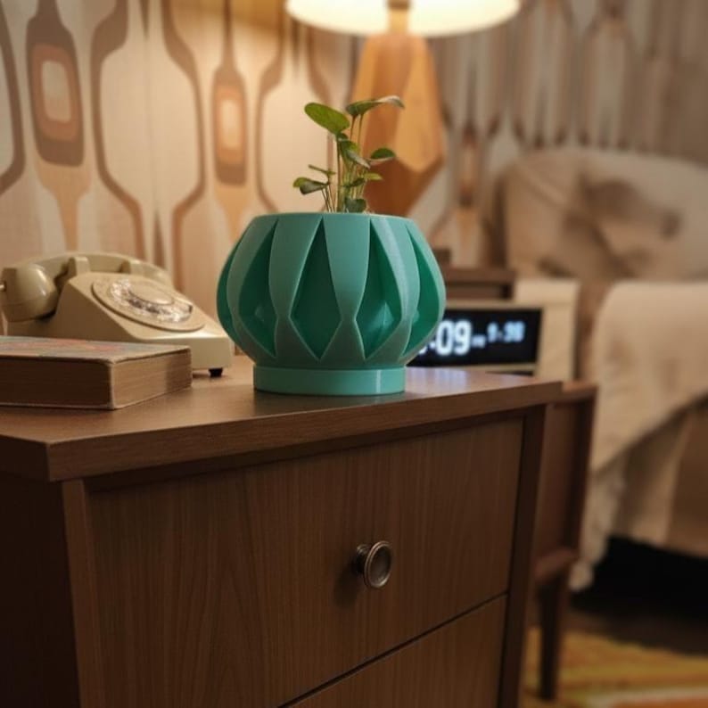 May include: A teal-colored, geometric-patterned planter with a small plant inside. The planter sits on a wooden nightstand with a drawer and a round metal knob. A vintage rotary phone and a book are also on the nightstand.