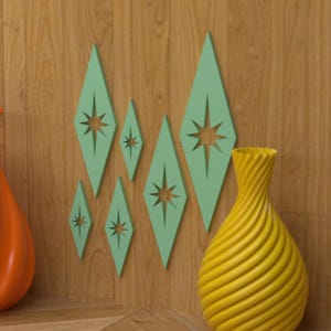 May include: A mid-century modern wall decor arrangement featuring six diamond-shaped, light green cutouts with starburst designs. A yellow, spiral-textured vase is on the right. The background is a wood-paneled wall.