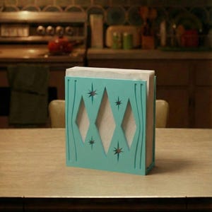 May include: A turquoise napkin holder featuring a cutout design of three vertical diamonds and four starburst shapes. The holder is constructed with a flat base and vertical sides, containing a stack of white paper napkins visible through the cutouts.