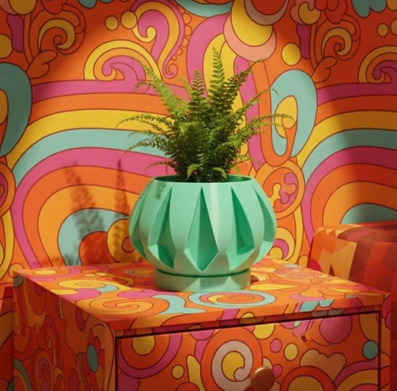 May include: A mint green, geometric-patterned planter pot holding a green fern plant. The pot sits on a colorful, patterned nightstand. The background features a vibrant, psychedelic wallpaper design with swirls of orange, pink, yellow, and blue.