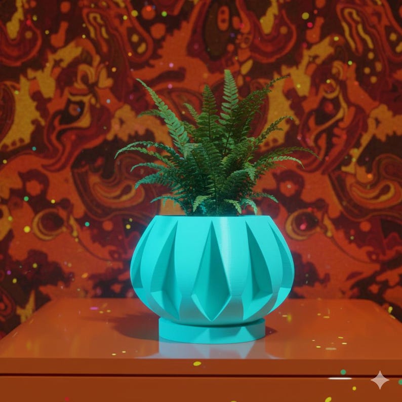 May include: A teal-colored, geometric planter pot with a fern plant inside. The pot has a faceted design and sits on a round base. The background features a patterned wallpaper in shades of orange, red, and yellow.