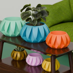 May include: A collection of colorful, geometric planters in shades of teal, blue, orange, gold, pink, and yellow. The planters have a unique, faceted design and are arranged on a dark wooden shelf. One planter holds a green plant.