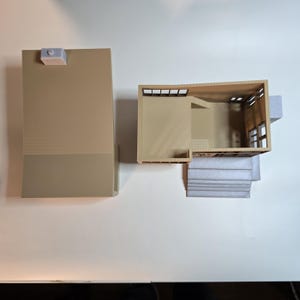May include: A 3D printed model of a house with a flat roof and a set of stairs leading up to the front door. The house is made of beige plastic and has a light gray roof.