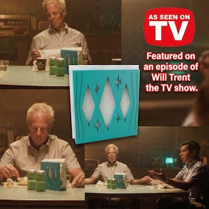 May include: A square teal napkin holder featuring a cutout pattern of three vertical diamonds and starburst shapes. The holder contains white paper napkins and is displayed alongside text stating AS SEEN ON TV and Featured on Will Trent.