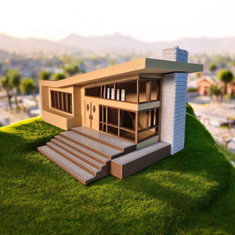May include: A model of a mid-century modern house with a flat roof, large windows, and a concrete chimney. The house is painted in shades of brown and beige and sits on a grassy hill.