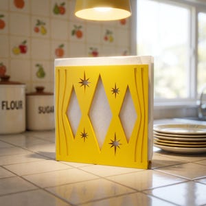 May include: A bright yellow napkin holder featuring a cutout design of three vertical diamonds and four starburst shapes. The holder is constructed with a flat base and holds a stack of white paper napkins, displaying a clean and geometric aesthetic.
