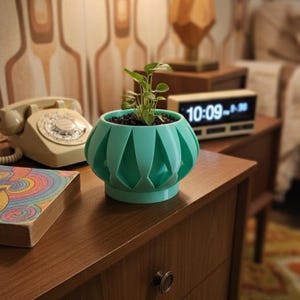 May include: A teal-colored, geometric-patterned planter pot with a small plant inside. The pot sits on a wooden surface, with a vintage rotary phone and a digital clock in the background. The pot has a unique, decorative design.