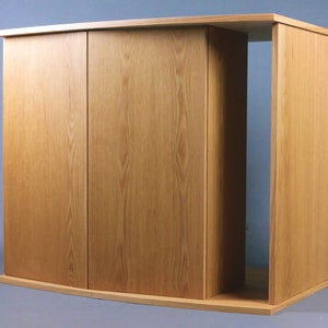 May include: A wooden cabinet with three doors and a curved base. The cabinet is made of light wood with a natural finish. The doors are closed and the cabinet is empty.