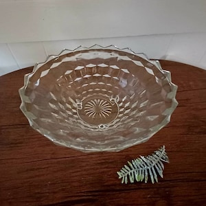 May include: A clear glass bowl with a diamond pattern and a scalloped edge. The bowl is sitting on a wooden surface.