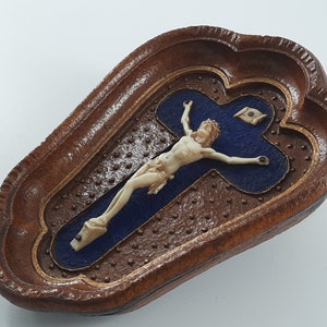 May include: A wooden box with a carved design and a blue velvet interior. The box contains a small ivory crucifix with a figure of Jesus Christ.