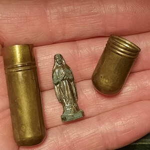 以下が含まれることがあります： 金色の小さな金属製の容器が3つあります。1つの容器は開いていて、他の2つは閉じています。開いている容器は円筒形で、丸みを帯びた上部があります。閉まっている容器は円筒形で、丸みを帯びた上部と底部があります。中央には、銀色の小さな金属製の女性の像があります。