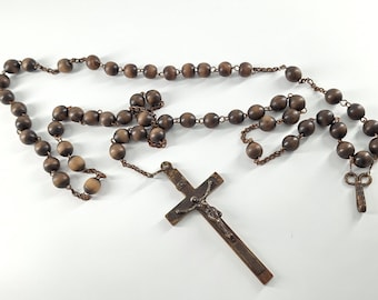 Könnte beinhalten: Ein Rosenkranz mit dunkelbraunen Holzperlen und einem Metallkruzifix. Die Perlen sind durch eine Kette verbunden. Das Kruzifix zeigt eine detaillierte Darstellung von Jesus Christus.