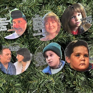 May include: Six round Christmas ornaments featuring characters from the movie Home Alone. Each ornament has a different character and a quote from the movie. The ornaments are white with a clear background.