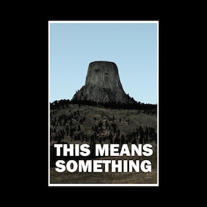 May include: A black and white photograph of a large rock formation, known as Devils Tower, rising from a grassy hill. The text "THIS MEANS SOMETHING" is printed in white letters at the bottom of the image.