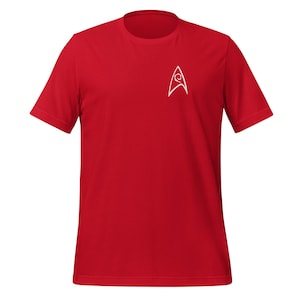 May include: A red short-sleeved t-shirt featuring a white Starfleet command insignia on the upper left chest. The emblem is a stylized delta shape with a curved line through the center. The shirt is made of a soft, likely breathable fabric.