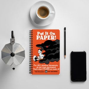 May include: A spiral bound notebook with an orange cover and the text "Put It On PAPER!" in black. The cover also features a black and white illustration of a person working on a computer with a shadowy figure behind them. The text "For ALL sensitive documents, do not trust electronics! That's what CYLONS are made of!" is printed below the illustration. The bottom of the cover includes the text "Colonial Ministry of Defense Office of War Information BUY WAR BONDS!"