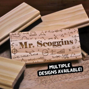 May include: Wooden chalkboard eraser with a math-themed design and the name "Mr. Scoggins" engraved on it. The eraser is made of natural wood and has a black sponge on the back. The text "MULTIPLE DESIGNS AVAILABLE!" is printed below the eraser.