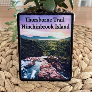 May include: A black and white patch with a photo of a waterfall and the text "Thorsborne Trail Hinchinbrook Island".