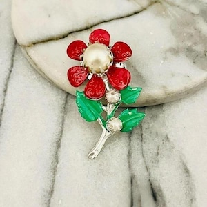 以下が含まれることがあります： パールを中央に、赤い花びらをあしらったヴィンテージのフラワーブローチ。ブローチは、緑の葉と、銀色の茎に小さなパールのアクセントが付いています。このフローラルアクセサリーは、クラシックなジュエリーです。