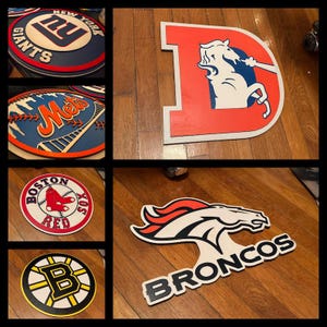 May include: A collection of six wooden signs featuring various sports team logos. The signs are painted in team colors and feature the team's name and logo. The logos include the New York Giants, New York Mets, Boston Red Sox, Denver Broncos, and the Boston Bruins.