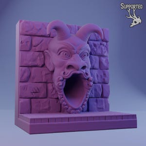 May include: A 3D printed miniature of a stone wall with a demonic face carved into it. The face is open-mouthed, revealing a tunnel inside. The miniature is painted in a purple color.