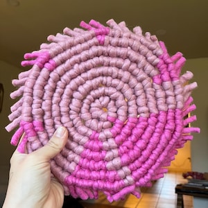 Könnte beinhalten: Ein runder Makramee-Wandbehang in Rosa und Pink mit Fransenrand.